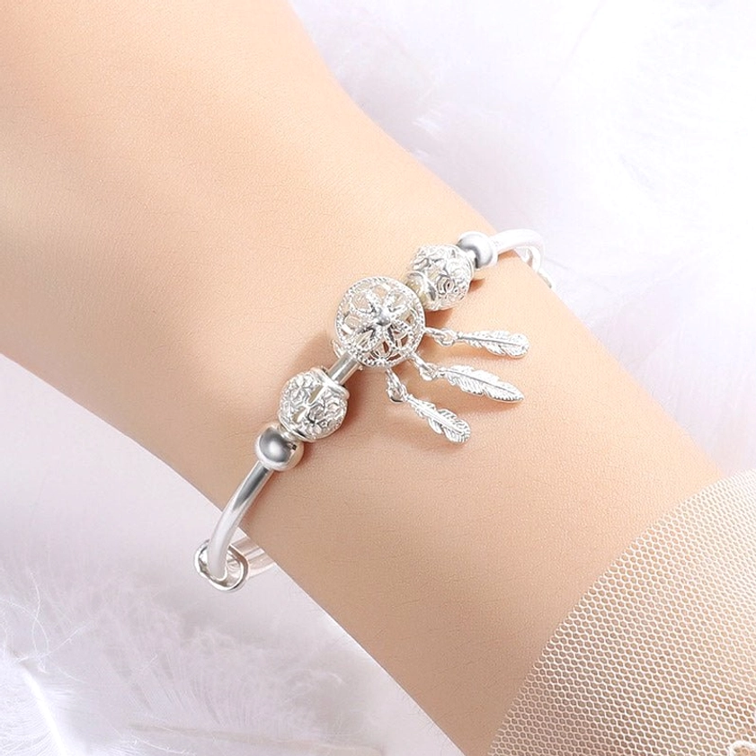 Minimalist silver dream catcher buddhist bracelet with feather tassel charms worn on light skin female wrist showing elegant side profile