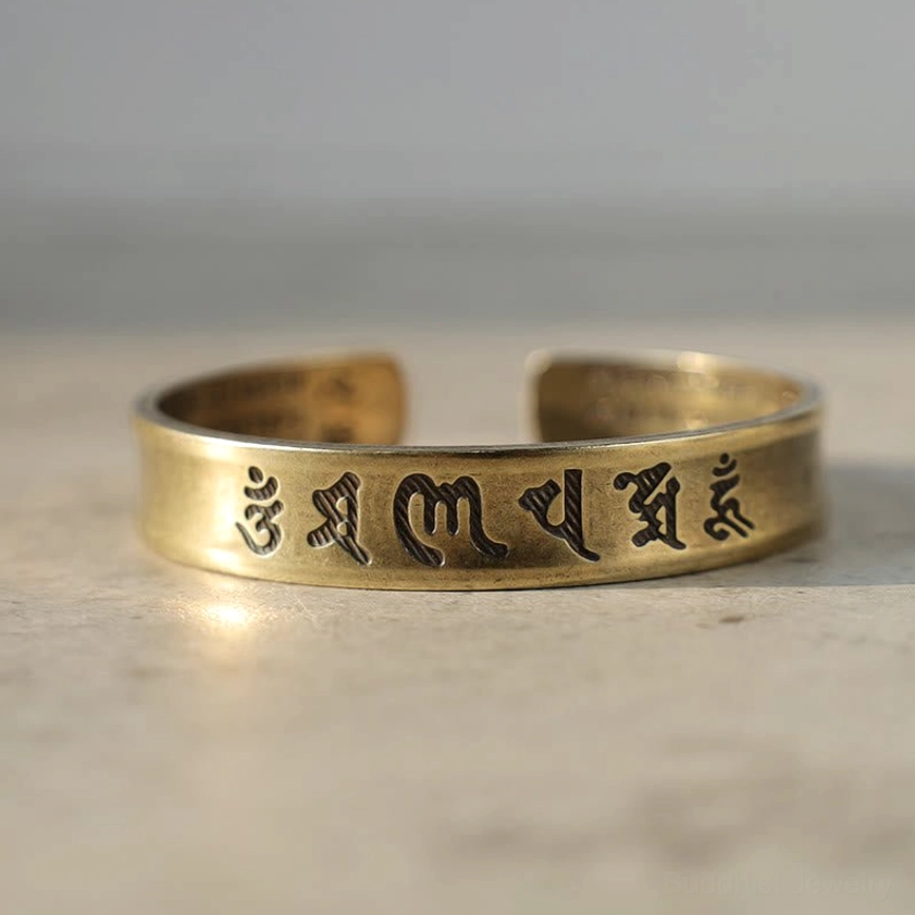 Open brass mantra cuff bracelet shown from low angle, highlighting curved band design and Sanskrit engraving