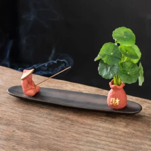 Orange Fisherman ceramic Buddhist incense burner with figurine and vase on wooden tea table with penny grass and smoking incense