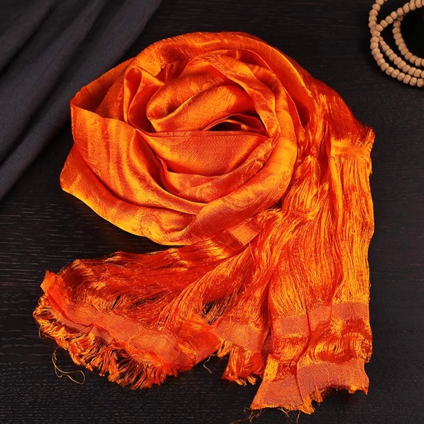 Warm orange Buddhist blessing khata scarf with frayed tassel ends on dark wooden background with meditation beads