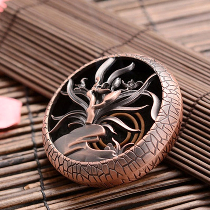 Orchid pattern brass incense burner with coil incense loaded inside, placed on bamboo mat, copper red cracked finish showing detailed hollow orchid lid carving