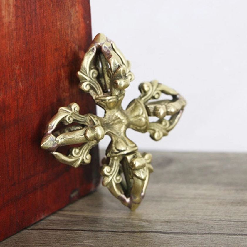 Copper vajra ornate four-pronged design side oblique angle showing aged bronze metal tone on wooden surface