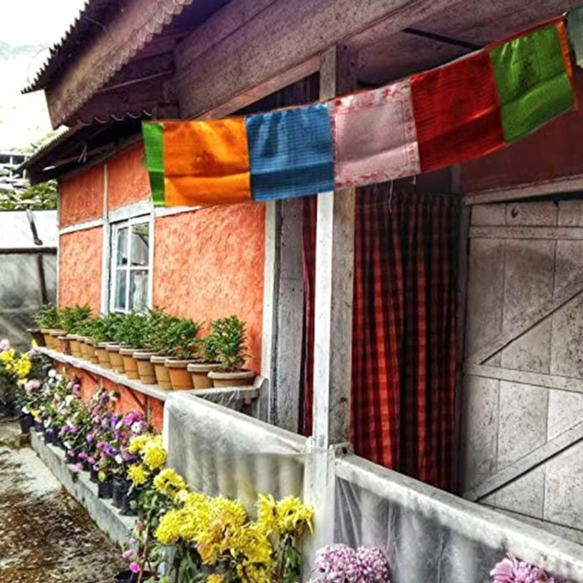 Buddhist prayer flags hung outdoors under residential eaves displaying vibrant multicolor rectangular panels with striped designs