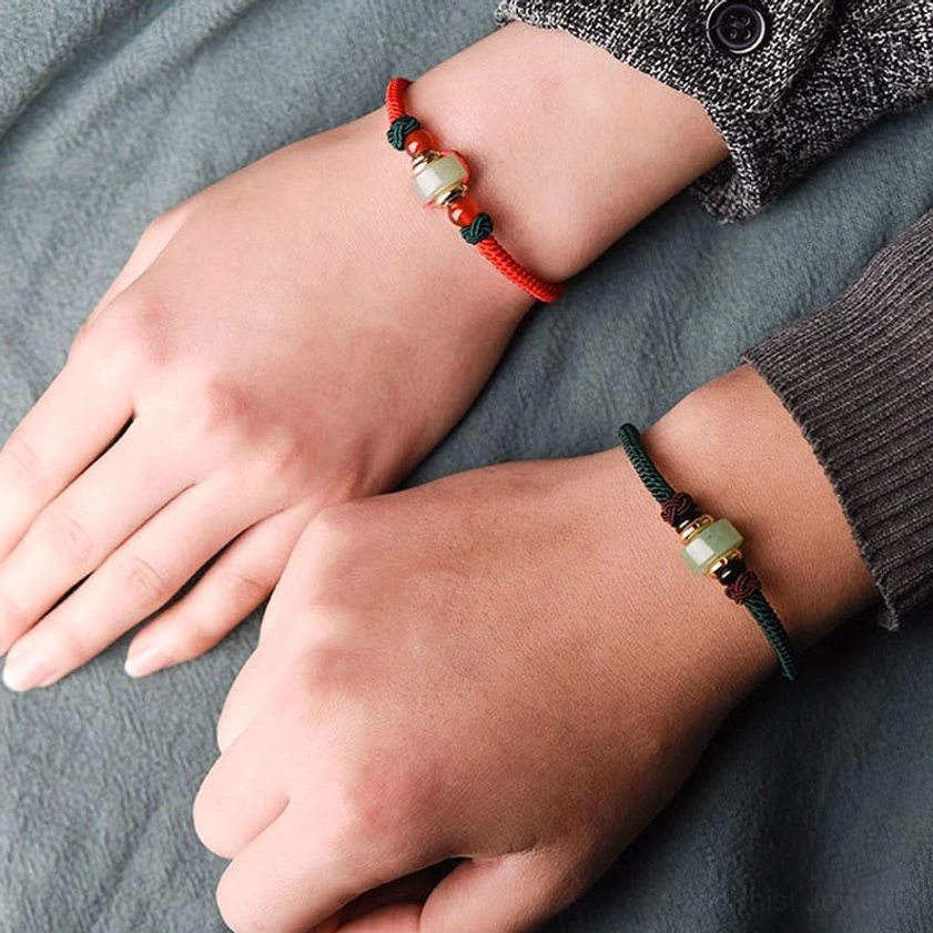 Two wrists wearing matching braided Buddhist luck bracelets with green aventurine and red agate combination