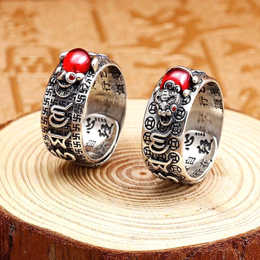 Pair of Buddhist wealth rings with Pixiu design, aged silver tone, red cabochon stones, overhead flat lay on wooden surface