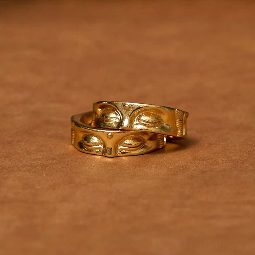 Two matching Buddha meditation copper rings with polished golden Buddha eye embossed designs on brown leather background overhead view
