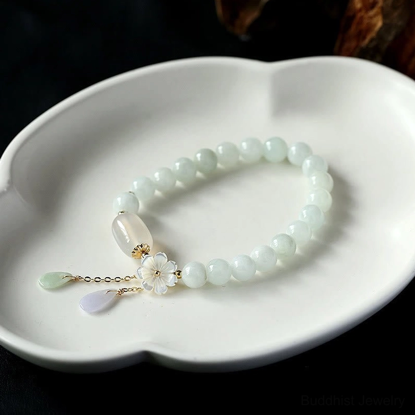 Pale jade Buddhist bracelet with decorative flower charm and dual drop pendants on ceramic tray