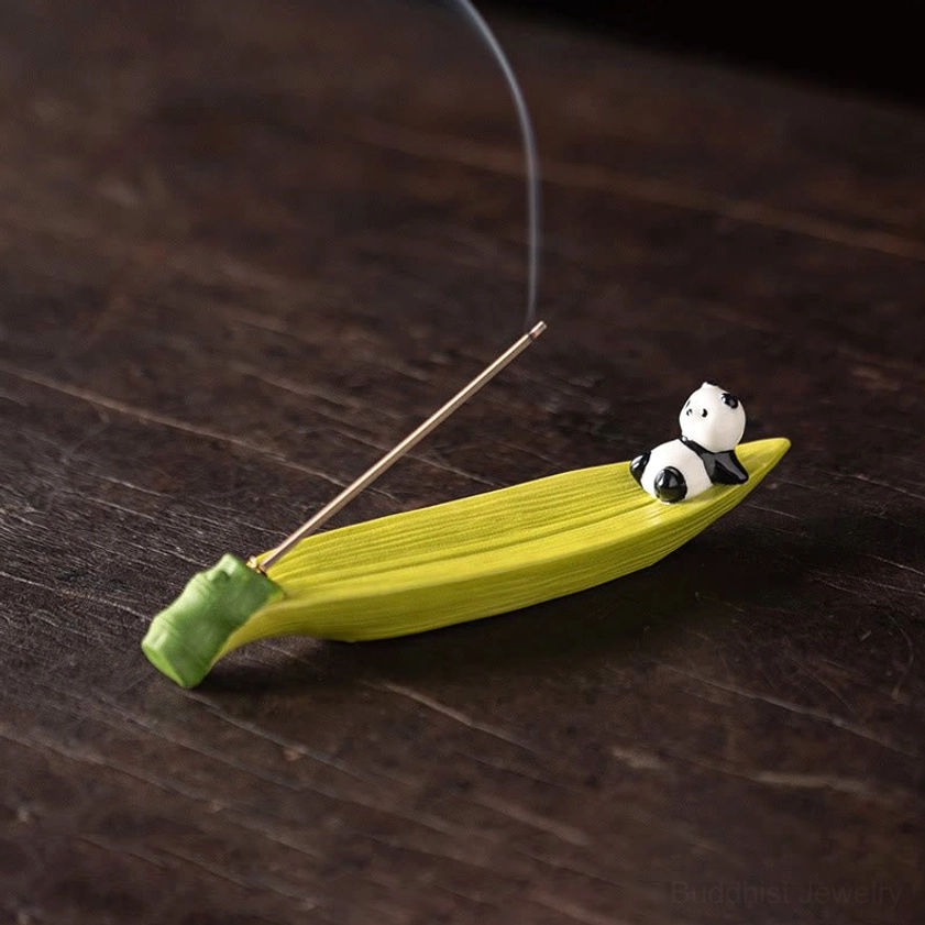 Green ceramic panda bamboo leaf incense burner on dark wooden table with lit incense stick, overhead view