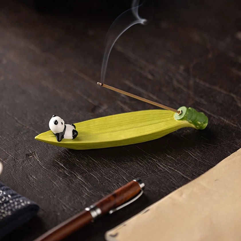 Ceramic panda lying on bamboo leaf incense burner on study desk with lit incense, eye-level side view