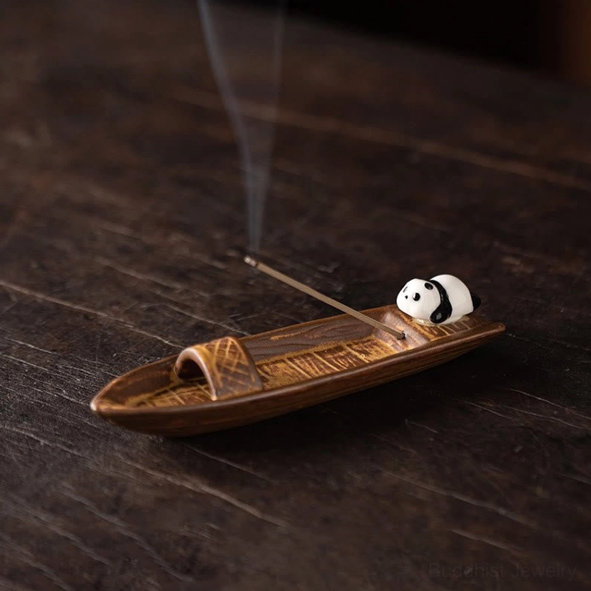 Ceramic panda boat incense burner on dark wood desk with lit incense and rising smoke, side view