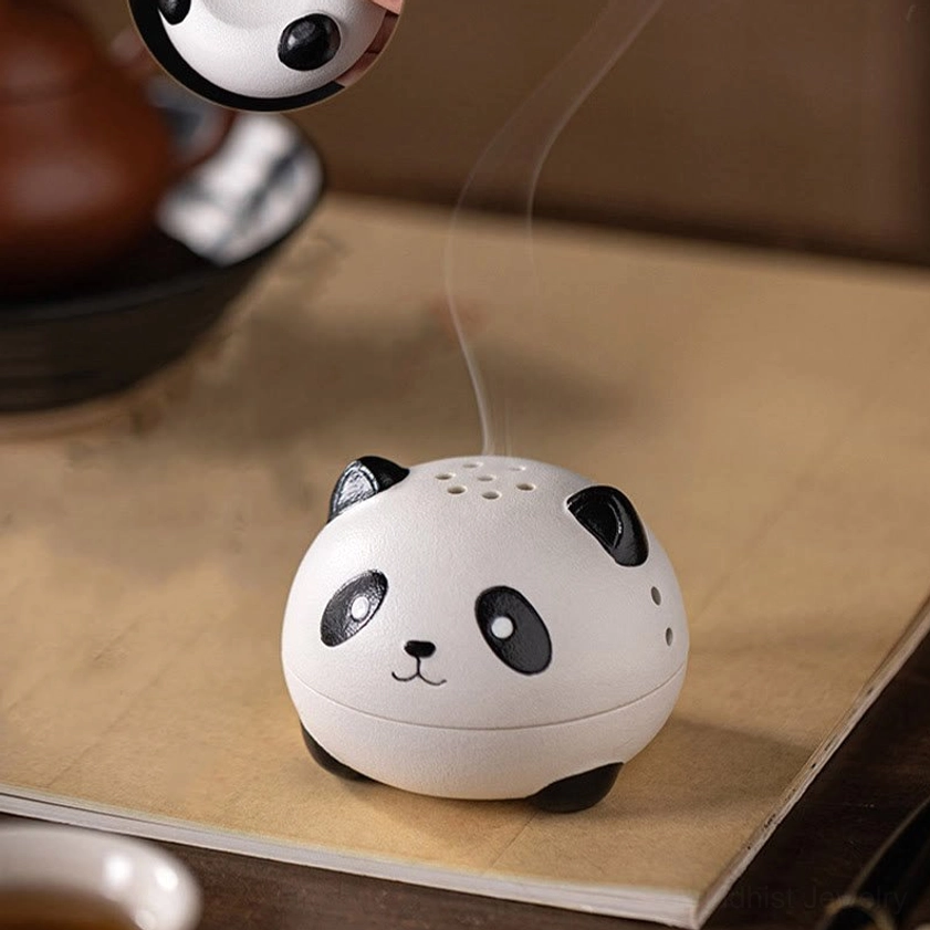 Panda-shaped incense burner on low wooden desk with kraft paper mat, showing active smoke with partial tea set in background