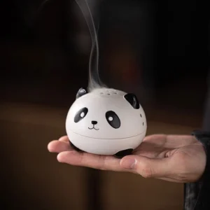 Handcrafted panda ceramic incense burner held in palm, showing matte white finish with black panda design and emitting fragrant incense smoke