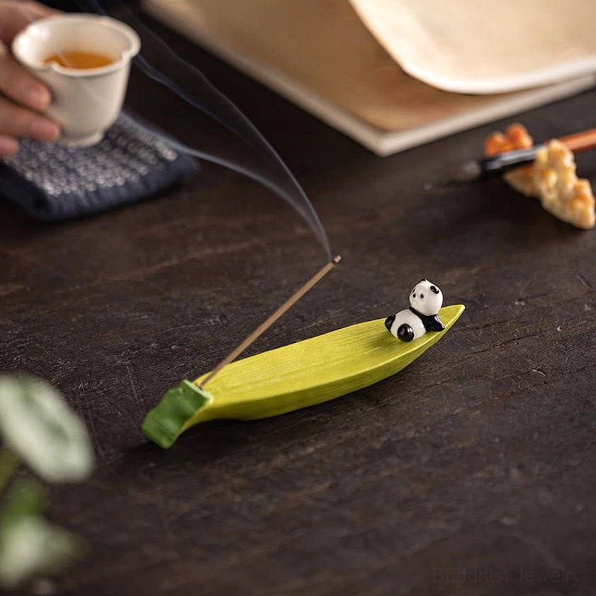 Panda bamboo leaf ceramic incense burner on tea desk with teacup and stationery, top-down view with burning incense