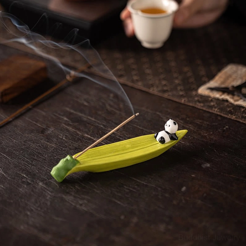 Green panda bamboo leaf incense burner on tea table with teacup and desk mat, high side view with smoking incense