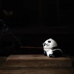 Panda ceramic incense burner with burning incense showing aromatic smoke from side angle - black and white handcrafted design on wooden table
