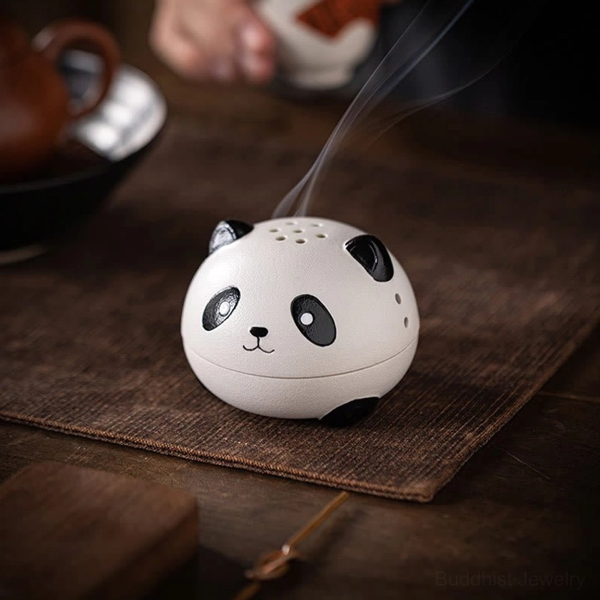 Three-quarter angle of panda-shaped ceramic incense burner on tea table with woven placemat, showing active incense burning