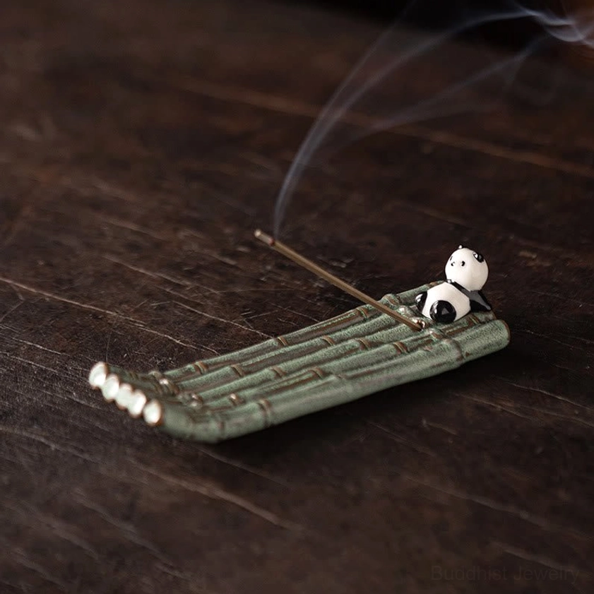 Ceramic panda lying on back incense holder on dark wood surface with lit incense, decorative tabletop view