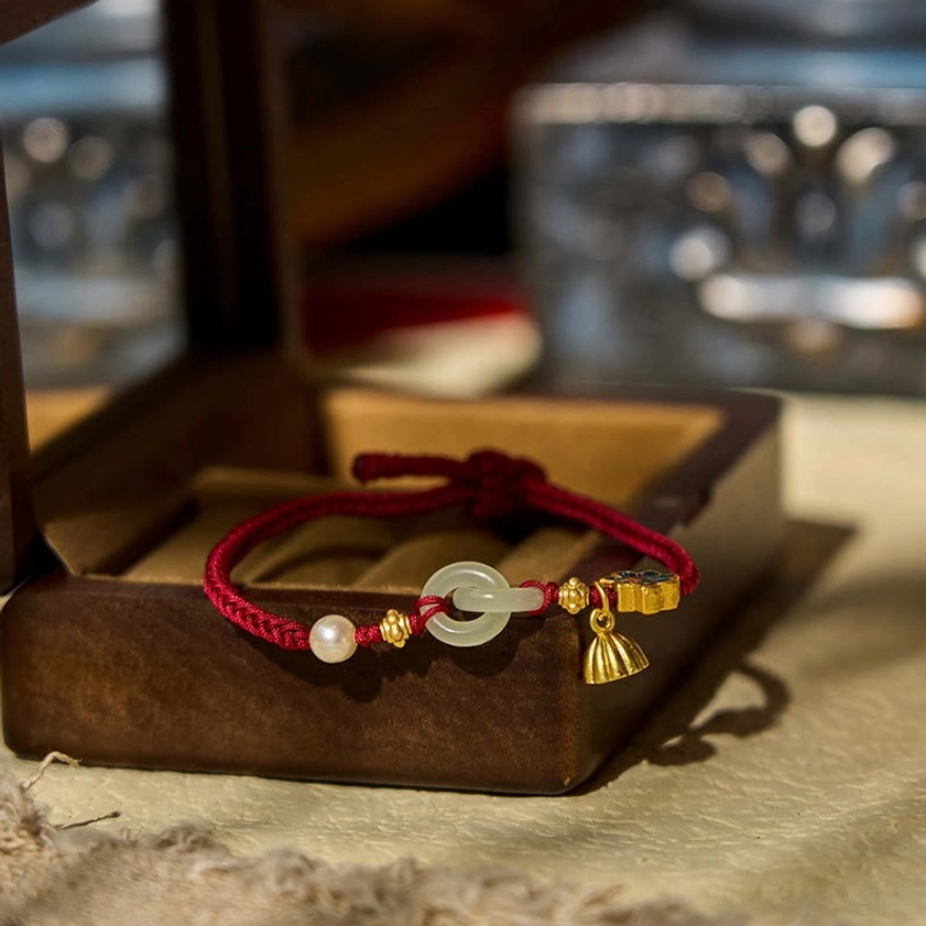 Hetian jade fortune bracelet with peace buckle displayed on wooden jewelry box, showing red rope and gold lotus charm