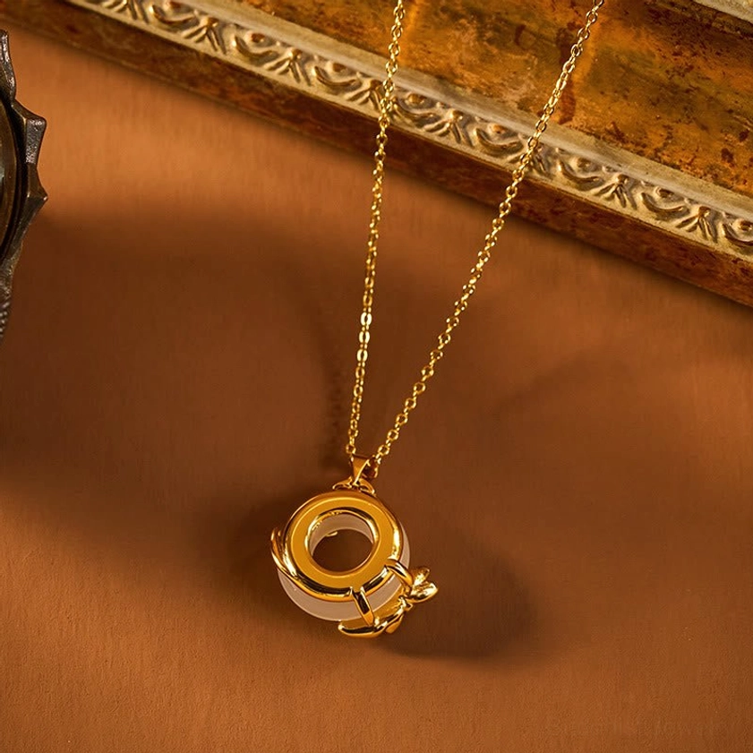 Buddhist peace buckle pendant close-up showing dual-ring design with gold inlay and white stone accent on luxury wooden surface