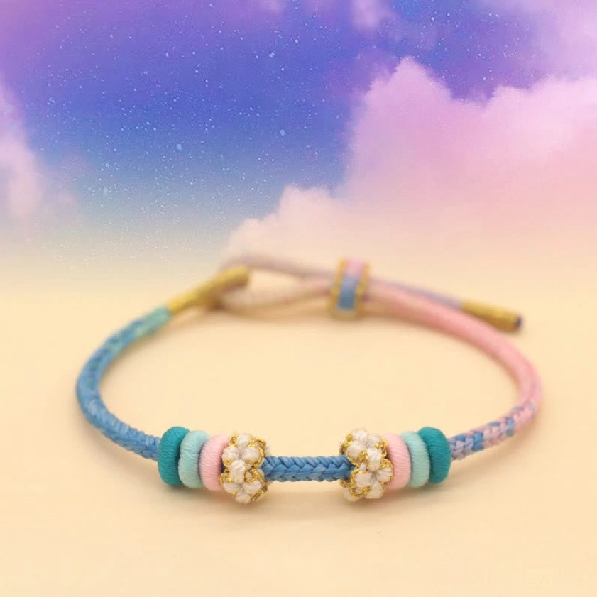 Pastel blue and pink Buddhist braided bracelet with flower bead charm on starry sky background