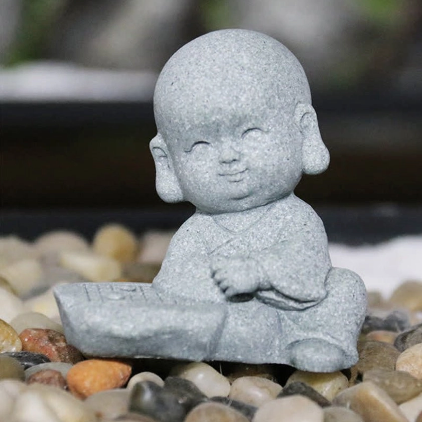 Serene sitting monk Buddha figurine with calm smiling expression on pebble stone background