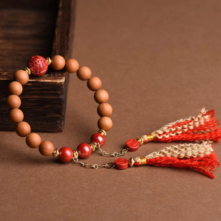 Smooth natural peach wood beads with carved red cinnabar bead and paired red tassels on craft paper and wooden block