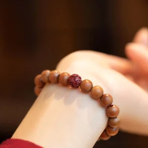 Peach wood and cinnabar lotus bracelet worn on wrist, showing natural wooden beads with carved red lotus accent bead