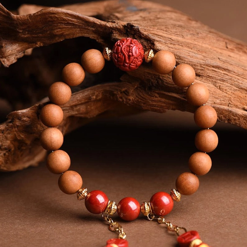 Close-up of intricately carved red cinnabar pixiu bead with polished natural peach wood beads and gold metal fasteners on driftwood