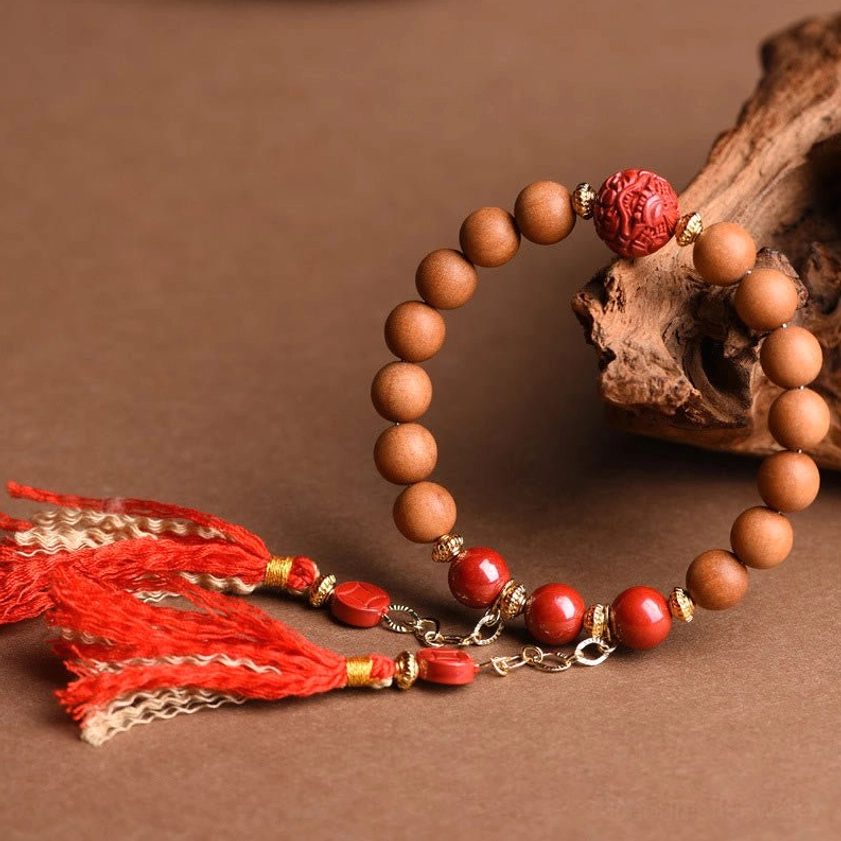 Natural peach wood beads with carved red cinnabar pixiu charm and decorative gold-trimmed red tassels on craft paper background