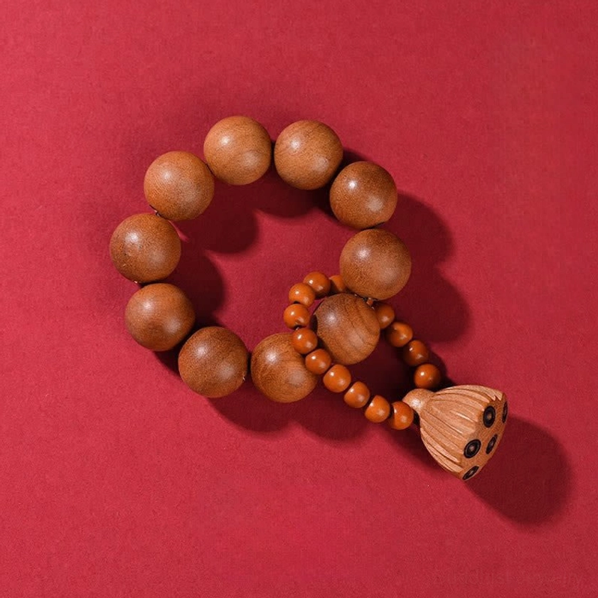 Flat lay of peach wood prayer beads with lotus pod charm on red background, showing smooth round wooden beads and carved lotus pendant details