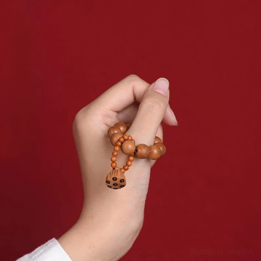Single hand gripping peach wood meditation beads with lotus pod tassel on red background, showing tactile grounding hold