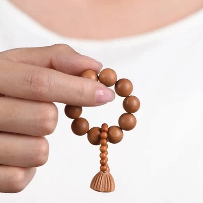 Close-up of hands holding peach wood lotus pod meditation mala beads with natural brown wooden texture and carved lotus charm pendant