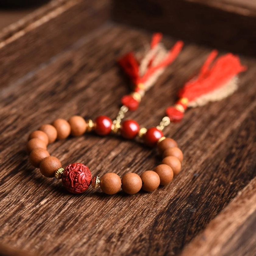 Round natural peach wood beads with red cinnabar accents and dual tassel charms arranged on dark wooden tabletop