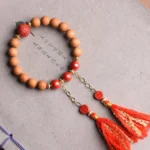 Handcrafted peach wood pixiu prosperity bracelet with red cinnabar beads and dual red tassels displayed on Chinese calligraphy paper