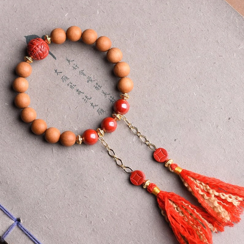 Handcrafted peach wood pixiu prosperity bracelet with red cinnabar beads and dual red tassels displayed on Chinese calligraphy paper