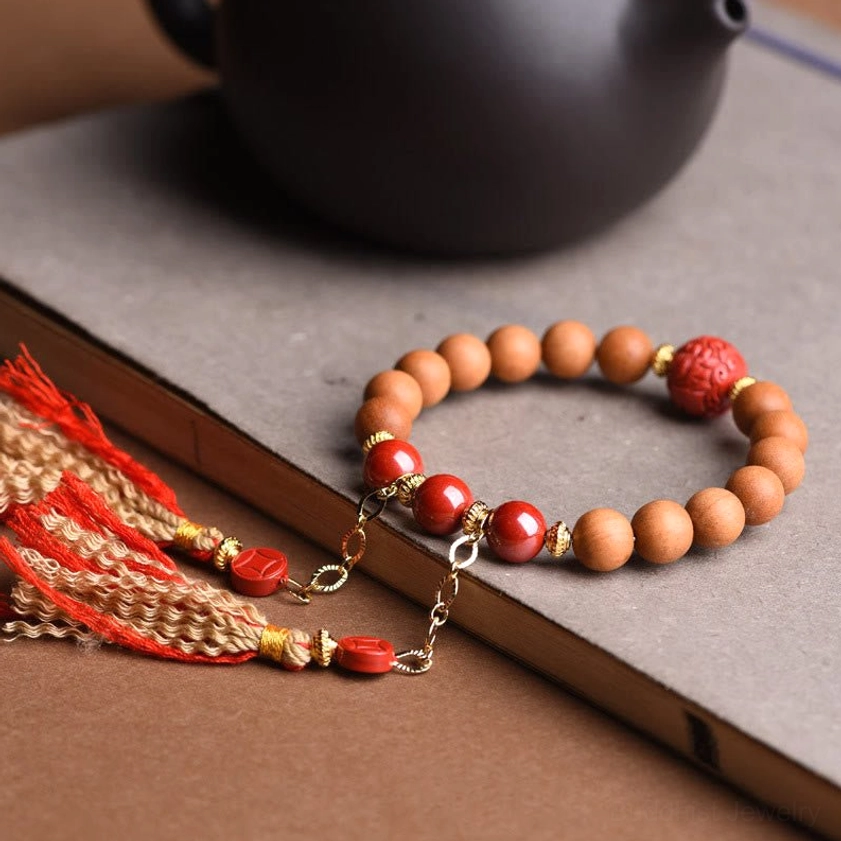 Peach wood pixiu bracelet with light brown wooden beads, red cinnabar spacer beads, and detachable tassel charms in oblique view