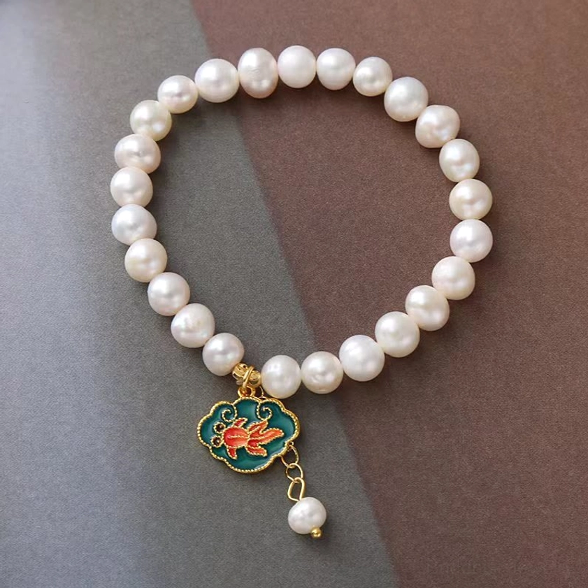 Pearl koi fish Buddhist charm bracelet on neutral tabletop, showcasing enameled koi pendant and luminous freshwater pearls for prosperity and good fortune