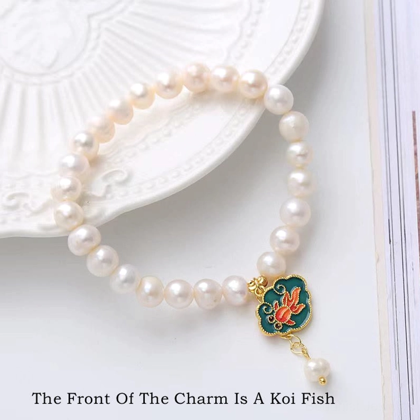 Close-up of pearl koi lotus bracelet displayed on white ceramic plate, showing detailed gilt enamel koi fish charm with freshwater pearl beads