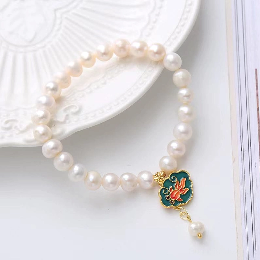 Angled view of pearl koi lotus bracelet on ceramic plate, displaying both sides of reversible charm with freshwater pearl and gilt metal details