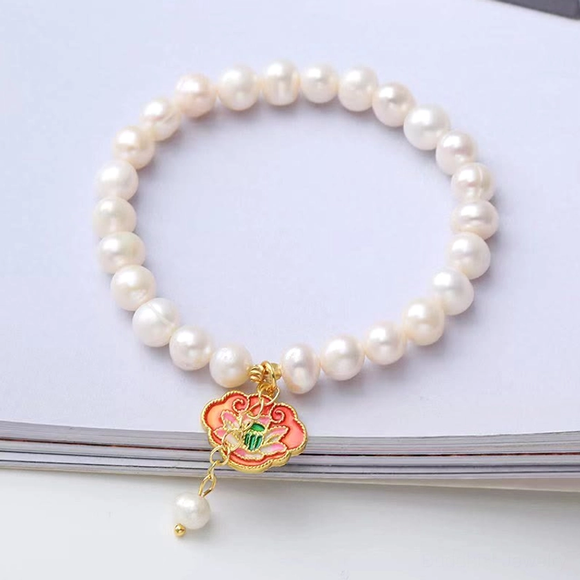 Pearl lotus flower Buddhist charm bracelet on magazine, featuring enamel lotus pendant with pearl beads, symbol of enlightenment and resilience