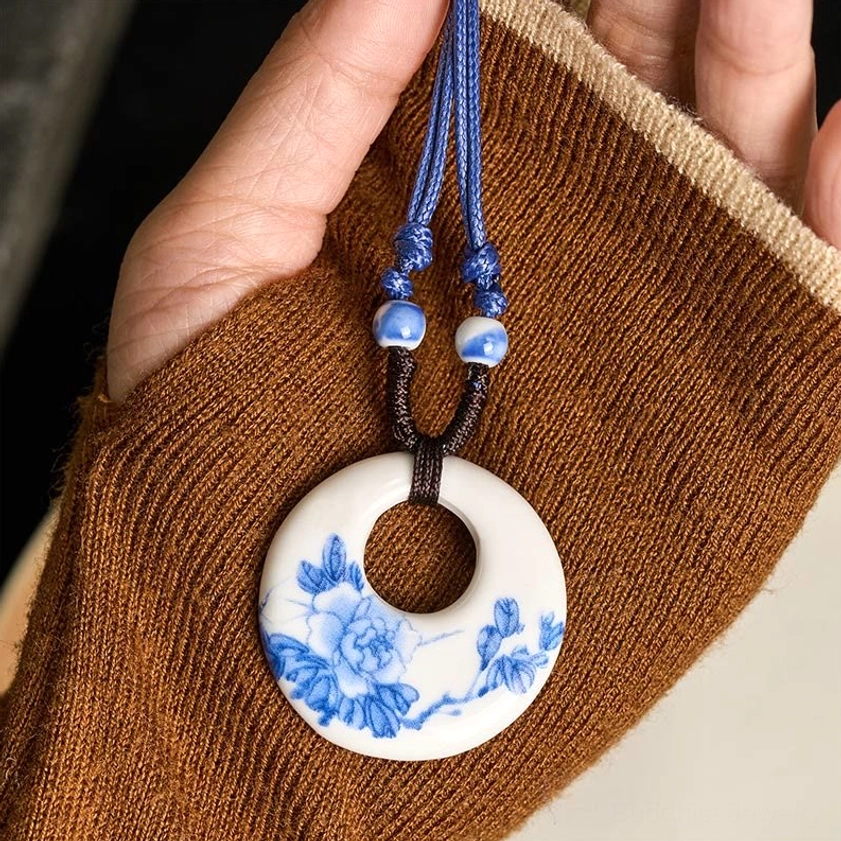 Peony and branch printed ceramic pendant necklace close-up handheld on brown knitted sweater background