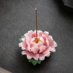 Pink peony ceramic incense burner with green leaves, top view on dark leather surface