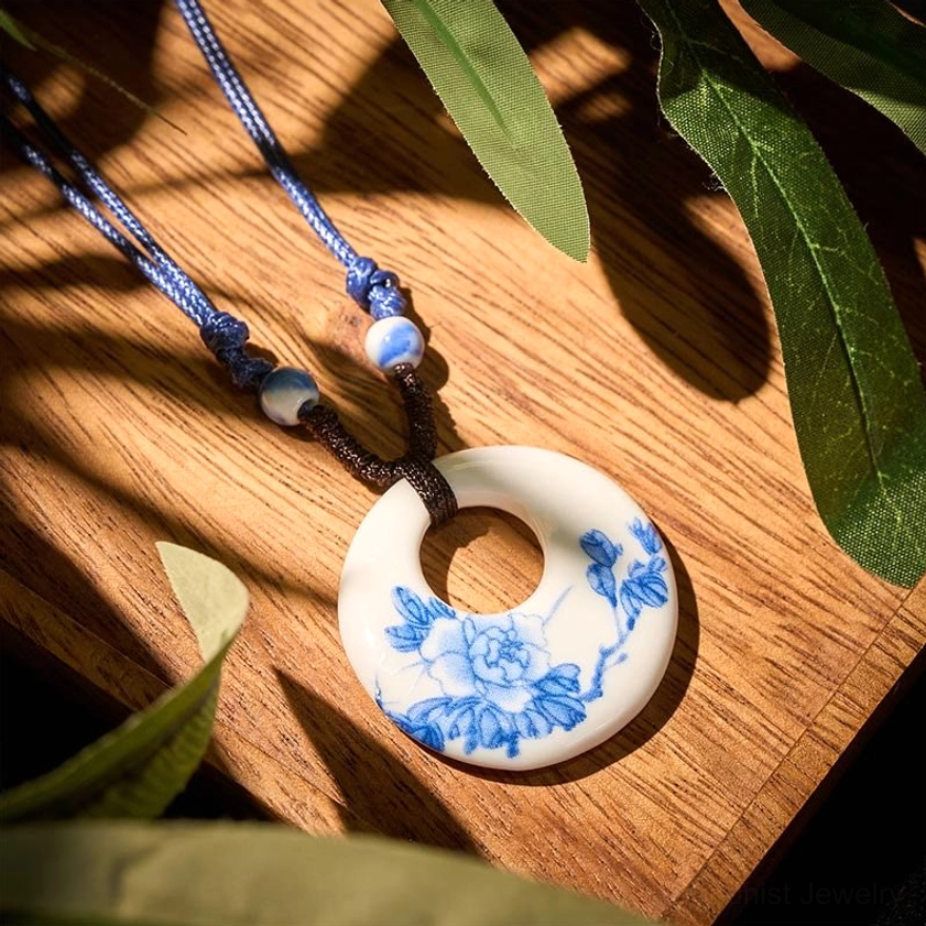 Peony flower printed ceramic pendant necklace overhead view on wooden table with green foliage