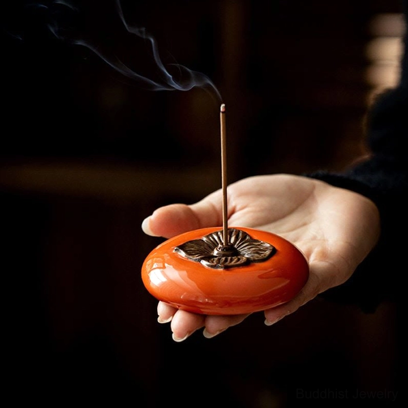 Persimmon ceramic incense burner with glowing incense stick and rising aromatic smoke in dim meditation setting