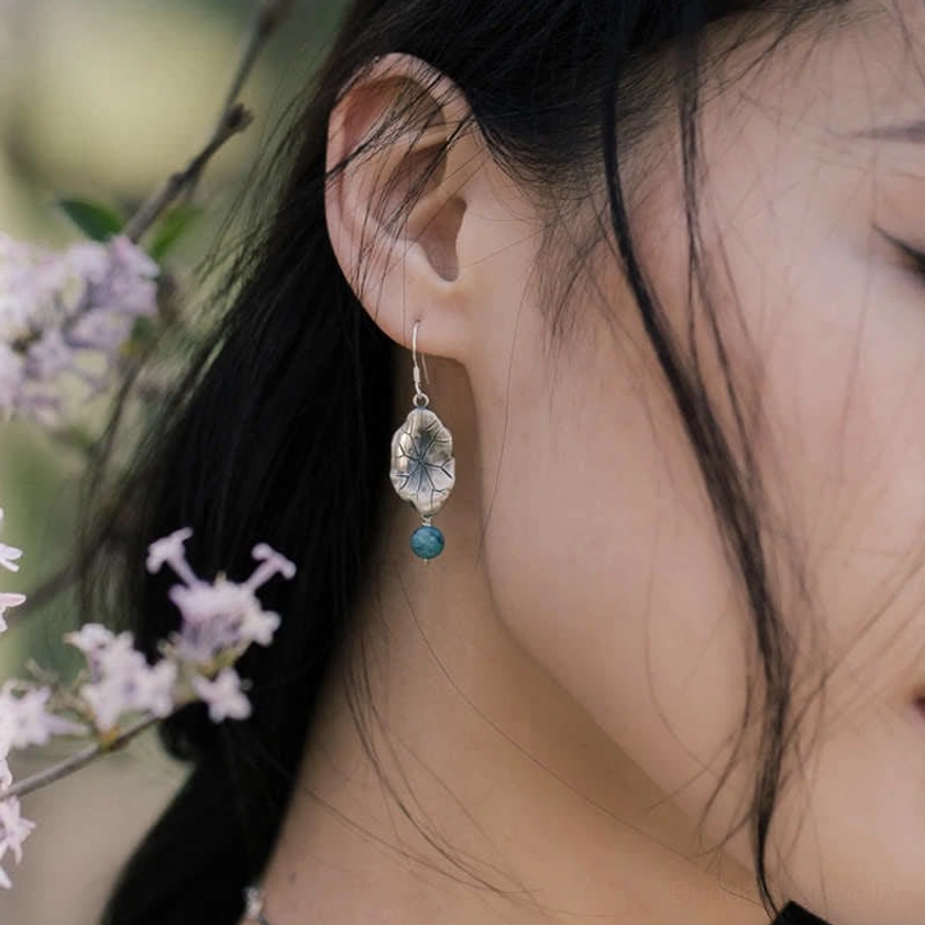 Delicate turquoise lotus leaf drop earrings worn outdoors with purple bloom background