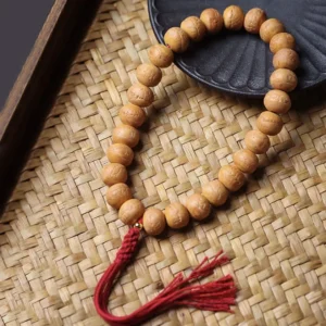 Phoenix Eye Bodhi mala bracelet flat lay on bamboo mat with red silk tassel, showing natural tan beads with eye markings