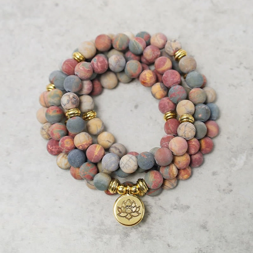 Picasso Jasper 108 mala beads bracelet with gold lotus charm on marble background, top-down flat lay view