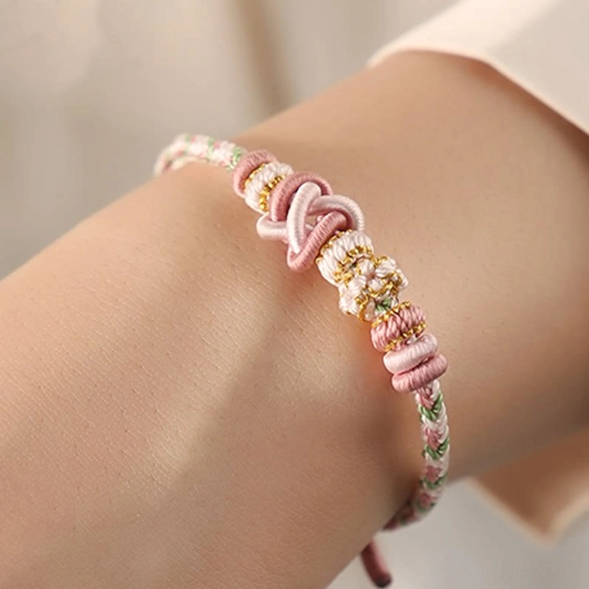 Pink Buddhist string bracelet worn on wrist showing woven knot design with gold details and adjustable comfortable fit