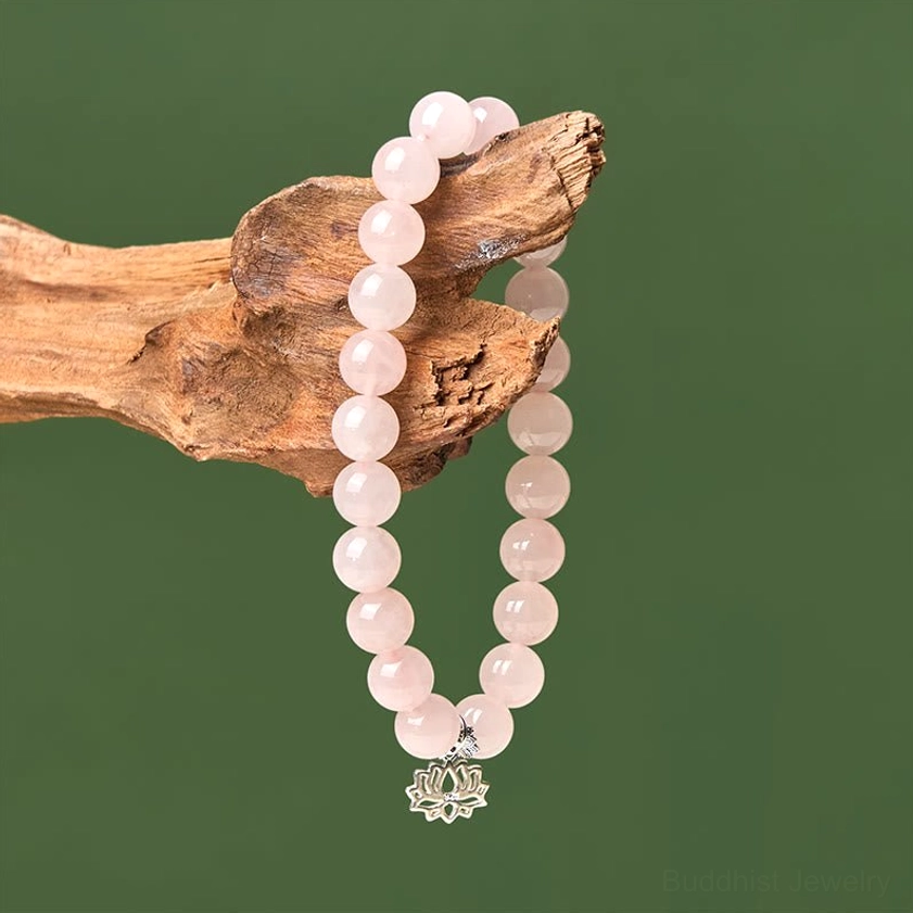 Pink crystal elastic bracelet with sterling silver lotus charm hanging on driftwood
