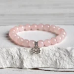 Pink crystal lotus charm bracelet with 925 sterling silver pendant displayed on stone with overhead view